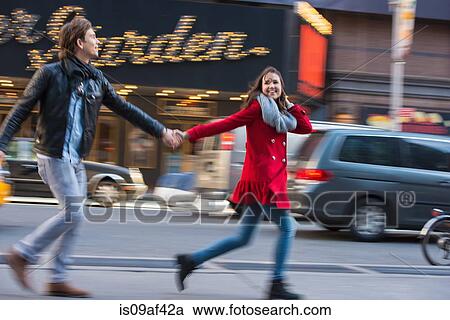 Stock Image - Young couple running along street, New York City, USA. Fotosearch