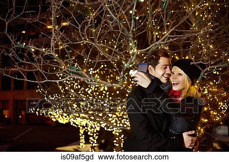 Stock Image - Young couple taking self portrait with city xmas lights. Fotosearch
