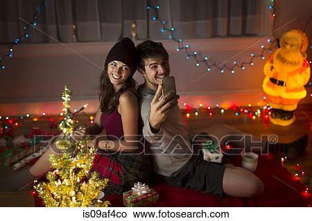 Picture - Young couple taking selfie in sitting room at christmas. Fotosearch