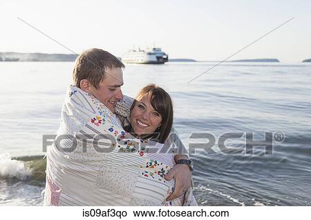 Picture - Young couple wrapped in a blanket at coast. Fotosearch