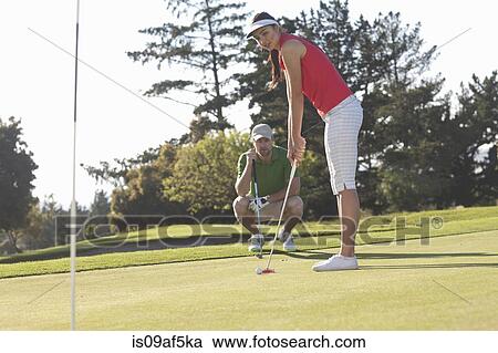 Stock Image - Young female golfer on golf course with trainer. Fotosearch