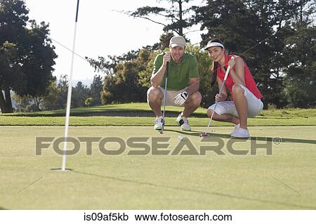 Stock Image - Young female golfer taking advice from trainer. Fotosearch