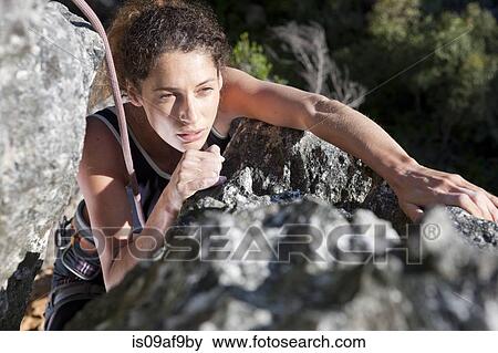 Stock Photo - Young female rock climber moving up rock face. Fotosearch
