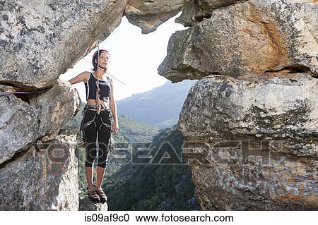Stock Image - Young female rock climber taking a break on rock ledge. Fotosearch