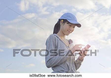Stock Image - Young female runner choosing music from MP3player. Fotosearch