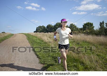 Stock Image - Young female runner running alongside dirt track. Fotosearch