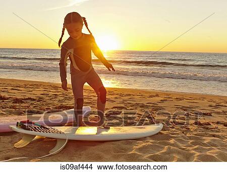 Young girl at beach wearing wetsuit and standing on surfboard View Large Photo Image Picture - Young girl at beach wearing wetsuit and standing on surfboard. Fotosearch