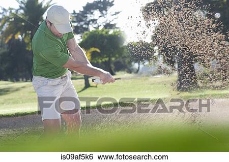 Stock Photograph - Young male golfer playing out of bunker. Fotosearch