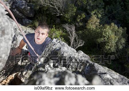 Young male rock climber watching and waiting on rock face View Large Photo Image Stock Photo - Young male rock climber watching and waiting on rock face. Fotosearch