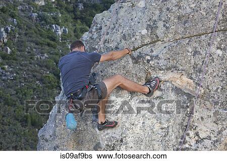 Young man climbing up rock face View Large Photo Image Stock Photograph - Young man climbing up rock face. Fotosearch