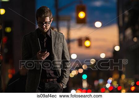 Stock Image - Young man strolling down street looking at mobile phone, Toronto, Ontario, Canada. Fotosearch