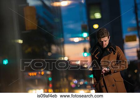 Stock Image - Young man waiting on street looking at watch, Toronto, Ontario, Canada. Fotosearch