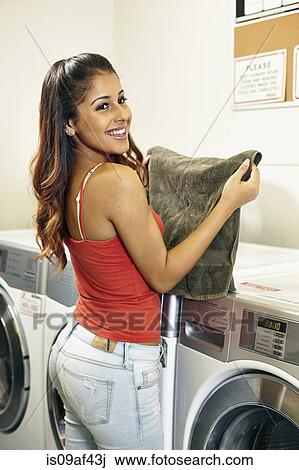 Stock Image - Young woman doing laundry in laundrette. Fotosearch