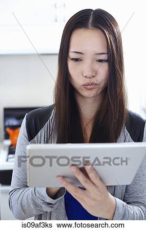 Stock Photograph - Young woman in kitchen reading digital tablet. Fotosearch