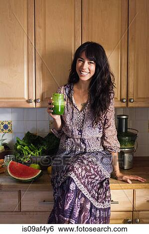 Stock Photograph - Young woman in kitchen with vegetable juice. Fotosearch