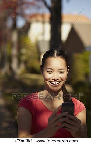 Stock Image - Young woman in sunshine looking at mobile phone. Fotosearch