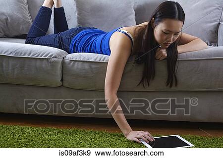 Young woman lounging on sofa using digital tablet View Large Photo Image Stock Photo - Young woman lounging on sofa using digital tablet. Fotosearch