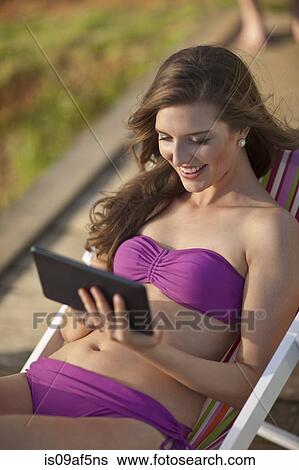 Stock Photograph - Young woman on deckchair looking at digital tablet. Fotosearch