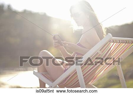 Young woman on deckchair texting from cellphone View Large Photo Image Stock Photograph - Young woman on deckchair texting from cellphone. Fotosearch