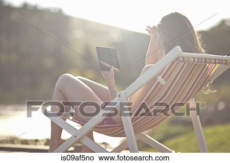 Young woman on deckchair using digital tablet View Large Photo Image Picture - Young woman on deckchair using digital tablet. Fotosearch