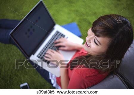 Stock Photography - Young woman sitting on rug typing on laptop. Fotosearch