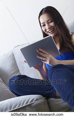 Young woman sitting on sofa using digital tablet View Large Photo Image Stock Image - Young woman sitting on sofa using digital tablet. Fotosearch