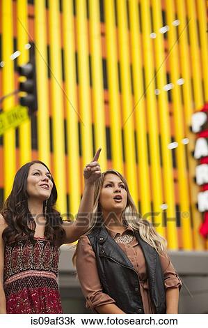 Stock Image - Young woman with friend in city pointing. Fotosearch