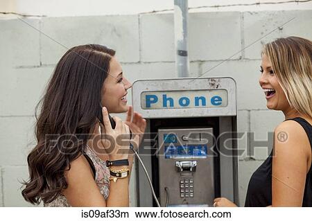 Picture - Young women using payphone laughing. Fotosearch