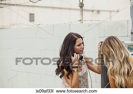 Stock Image - Young women using payphone. Fotosearch