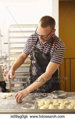 Stock Image - Male baker shaping dough in bakery. Fotosearch