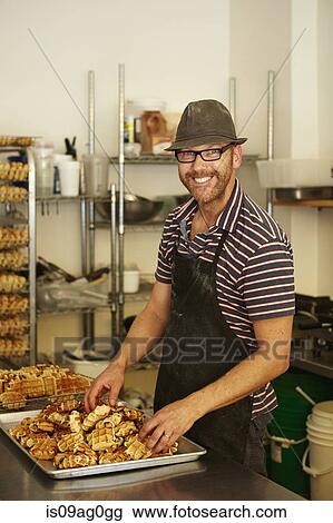 Stock Image - Male baker with tray of waffles in bakery. Fotosearch