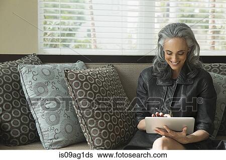 Stock Photograph - Woman using digital tablet on sofa. Fotosearch