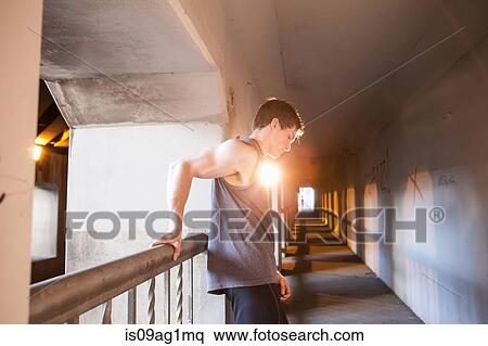 Stock Photography - Young male runner taking a break on urban bridge. Fotosearch