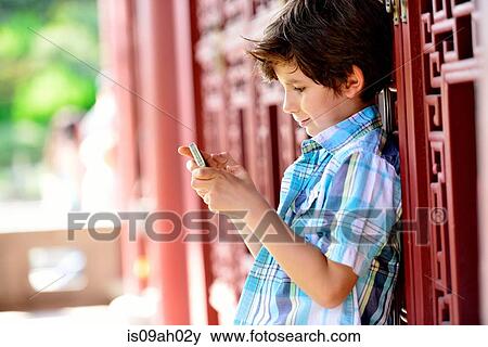 Boy leaning against red door texting on cellphone View Large Photo Image Stock Photo - Boy leaning against red door texting on cellphone. Fotosearch