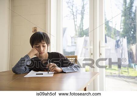 Stock Image - Boy sitting at table, holding pen to paper. Fotosearch