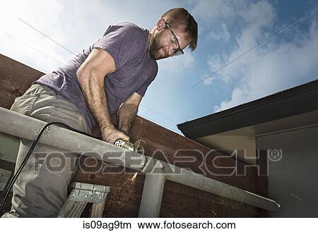 Picture - Builder on ladder sawing metal piping. Fotosearch