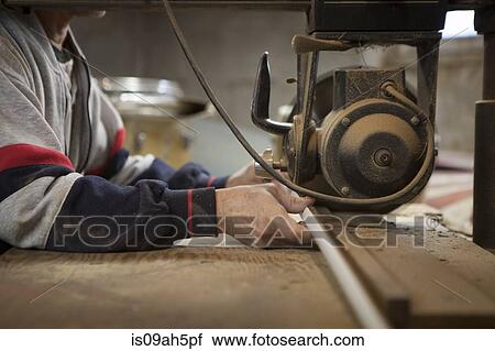 Stock Image - Close up of man using radial arm saw in workshop. Fotosearch