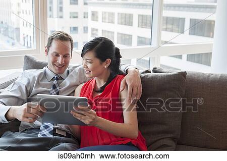 Couple relaxing on sofa using digital tablet View Large Photo Image Stock Image - Couple relaxing on sofa using digital tablet. Fotosearch