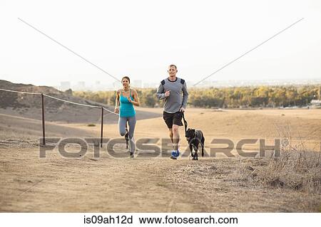 Stock Image - Couple running with dog. Fotosearch
