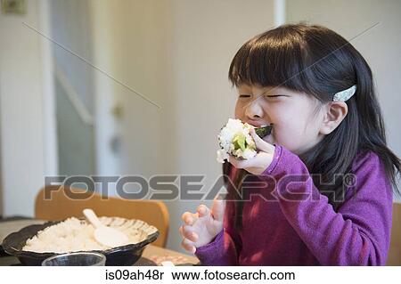 Stock Photography - Girl eating large rice parcel at dining table. Fotosearch