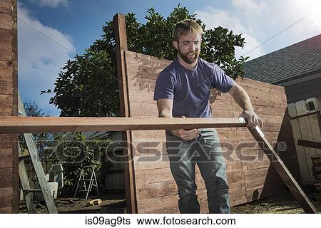 Stock Photograph - Joiner in backyard lifting wood framework. Fotosearch