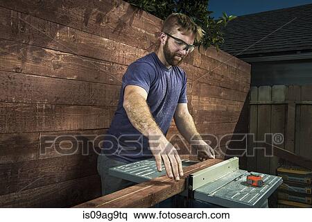 Stock Photography - Joiner in backyard lining up planks of wood on workbench. Fotosearch