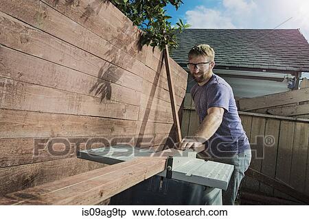 Stock Photography - Joiner in backyard measuring planks of wood on workbench. Fotosearch