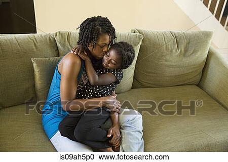 Stock Image - Mature woman and daughter hugging on sofa. Fotosearch