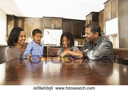 Stock Image - Mid adult couple and children playing draughts at table. Fotosearch
