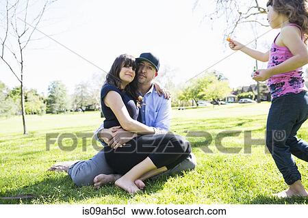 Stock Image - Mid adult couple sitting in the park with young daughter. Fotosearch