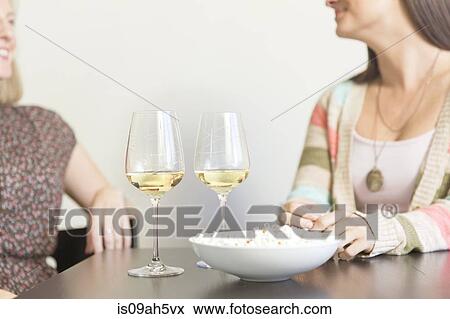 Mid adult female friends drinking at table with wine and popcorn View Large Photo Image Stock Photo - Mid adult female friends drinking at table with wine and popcorn. Fotosearch