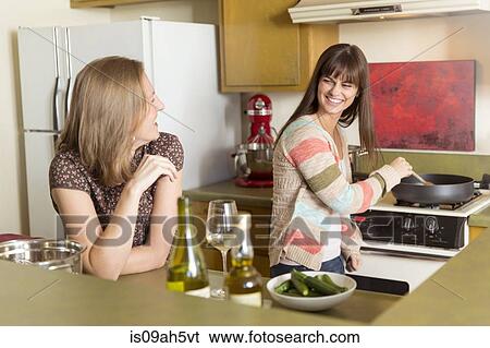 Stock Photograph - Mid adult female friends preparing food in kitchen. Fotosearch