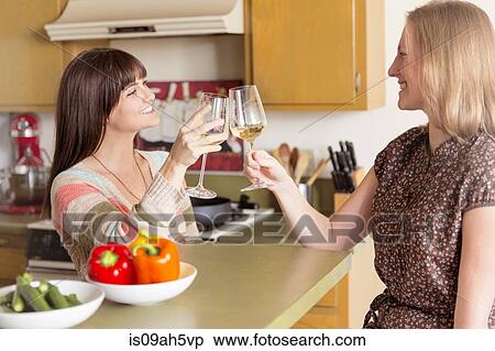 Mid adult female friends raising a glass in kitchen View Large Photo Image Stock Photography - Mid adult female friends raising a glass in kitchen. Fotosearch
