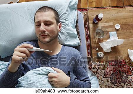 Mid adult man lying in bed looking at thermometer reading View Large Photo Image Stock Image - Mid adult man lying in bed looking at thermometer reading. Fotosearch